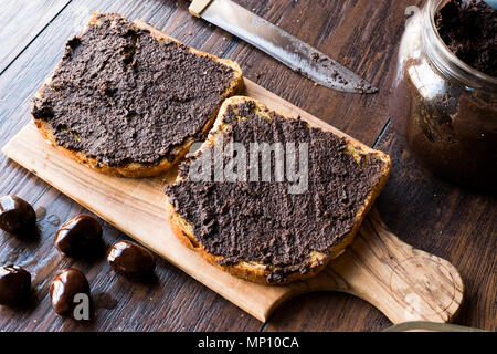 Nero oliva Tapenade su pane con coltello e Jar. Alimenti biologici. Foto Stock