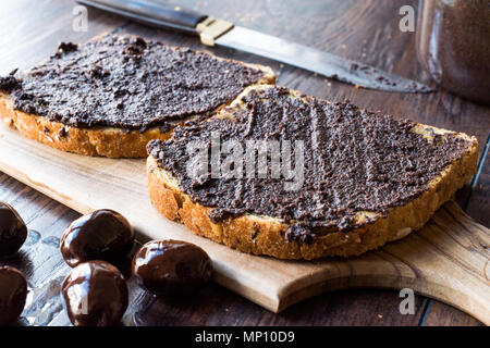 Nero oliva Tapenade su pane con coltello e Jar. Alimenti biologici. Foto Stock