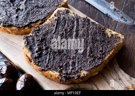 Nero oliva Tapenade su pane con coltello e Jar. Alimenti biologici. Foto Stock