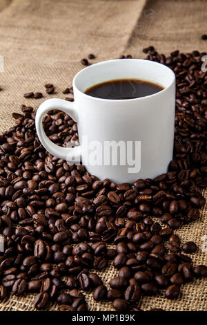 White tazza da caffè con i chicchi di caffè sul sacco di Hesse stoffa Foto Stock