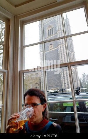 Una donna di bere una pinta in Sun Inn inDedham, con Dedham e chiesa parrocchiale visto attraverso la finestra Foto Stock