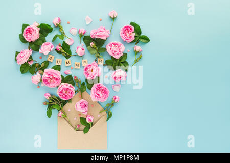 Close up reative layout con rosa tea rose fiori, foglie verdi candy cuori volare al di fuori della carta craft busta su fondo azzurro. Estate di parole scritte da lettere di legno. Spazio di testo. Foto Stock