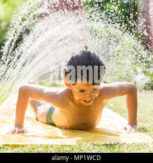 Ragazzo il raffreddamento con tubo flessibile da giardino, famiglia in background Foto Stock