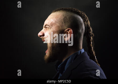 Uomo con dreadlocks urla in una rabbia, assomiglia a un viking, Iroquois haircut Foto Stock