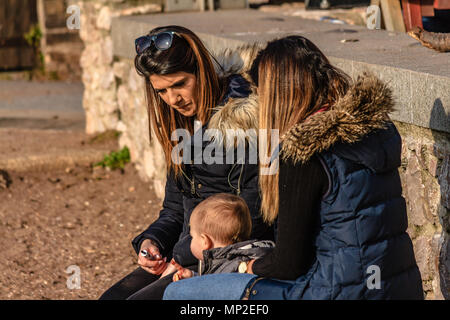 Due donne con un bambino che indossano tuniche e seduto sulla spiaggia. Teignmouth, Devon. Feb 2018. Foto Stock