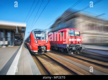 Treno ad alta velocità e il vecchio treno in movimento sulla stazione ferroviaria al tramonto. Moderno treno intercity sulla linea ferroviaria piattaforma. Paesaggio industriale. Organi giurisdi Foto Stock