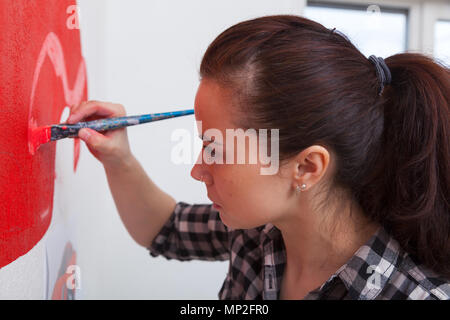 Giovani dai capelli scuri artista femminile in plaid shirt disegna su un muro bianco una grande macchina da scrivere rossa in un ragazzo in camera. Mom disegnare una spazzola con suo figlio in auto. Foto Stock