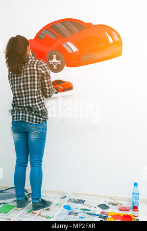 Close-up di una giovane donna artista e la madre del ragazzo per il disegno di un bambino su un muro bianco un bel rosso auto in una luce stanza dei bambini, sul pavimento giace Foto Stock