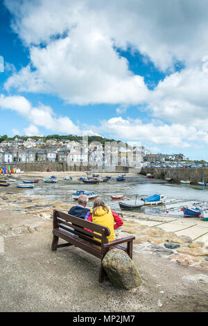 Vacanzieri relax sui posti a sedere con vista porto Mousehole in Cornovaglia. Foto Stock