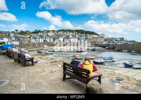 Vacanzieri relax sui posti a sedere con vista porto Mousehole in Cornovaglia. Foto Stock