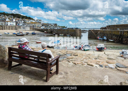 Vacanzieri relax su una sede che si affaccia sul porto Mousehole in Cornovaglia. Foto Stock