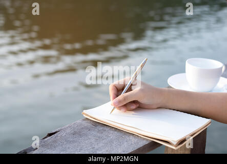 La scrittura a mano su notebook con caffè sul balcone di legno vicino al fiume Foto Stock