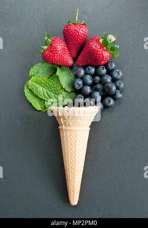 Freschi ingredienti naturali versando al di fuori di un cono gelato comprendente le fragole, menta e mirtilli Foto Stock