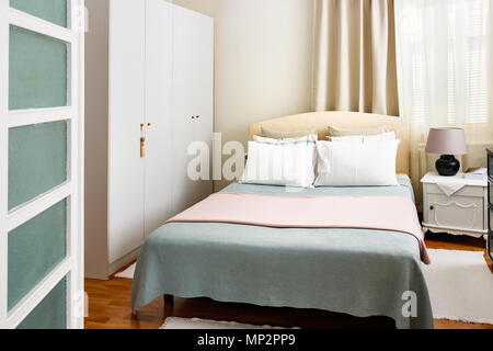 Camera da letto con letto matrimoniale con sei cuscini e un bianco in legno comodino con una lampada e libri. Foto Stock