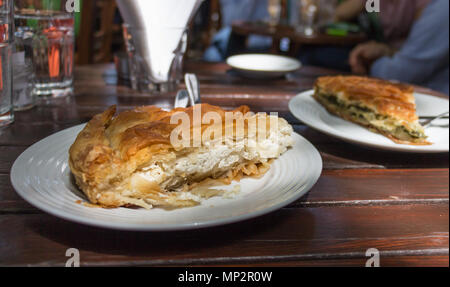 Primo piano di un pezzo di tiropita, un tradizionale formaggio greco la torta su un tavolo all'aperto. Foto Stock