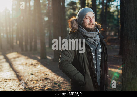 Ritratto, close-up di giovani gravi elegantemente con barba vestito in rgreen giacca invernale con un cappuccio e pelliccia sulla sua testa si erge contro il retro Foto Stock