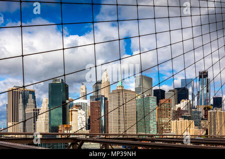 La skyline di Manhattan come visto attraverso la maglia del Ponte di Brooklyn a New York City, Stati Uniti d'America.