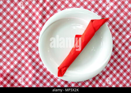 Piastra di colore bianco con posate wraped in rosso tovagliolo sulla tavola a scacchi panno Foto Stock