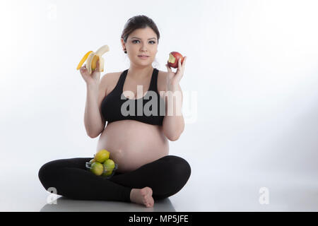 Un sano donna incinta di mangiare la vitamina ricchi frutti su sfondo bianco Foto Stock