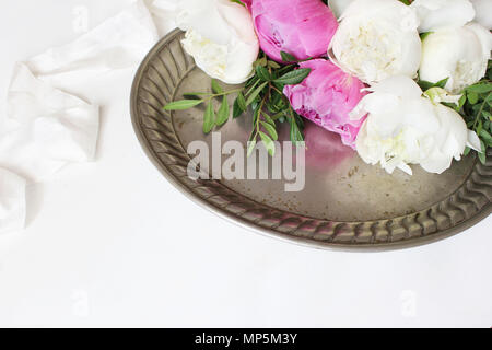 Elegante stock photo. Nozze femminile o tabella di compleanno con composizione floreale. Bianco e rosa peonie fiori sul vecchio vintage vassoio d'argento e nastro di seta. Sfondo bianco. Foto per il blog. Foto Stock