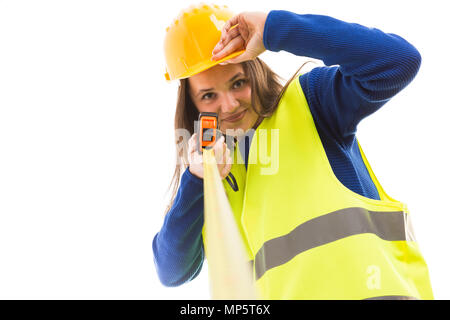 Giovane femmina attraente un architetto o un ingegnere azienda nastro di misurazione e toccando il casco come happy builder concetto isolato su sfondo bianco Foto Stock