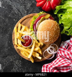 Gustosa burger con carne di manzo, patatine fritte e ketchup su sfondo scuro. Burger vista dall'alto. Il fast food patatine fritte fatte in casa e cheeseburger. Raccolto di quadrati Foto Stock