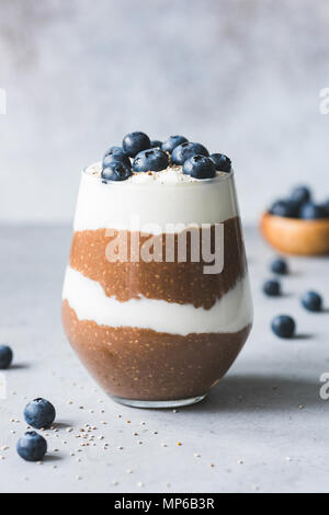 Stratificato budino di Chia o sana colazione parfait di cioccolato, yogurt, i mirtilli in un bicchiere su sfondo di calcestruzzo. Copia spazio per il testo Foto Stock