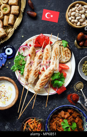 Turco Tradizionale o kebab kabob, dolciumi turchi, yogurt e salsa di verdure arrosto. Cibo turco bandiera su sfondo scuro. Vista superiore, vert Foto Stock