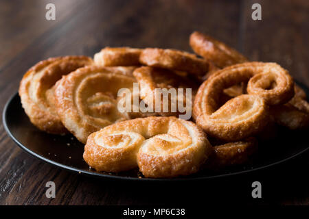 Palmier i cookie nella piastra nera su una superficie di legno. Concetto di dessert. Foto Stock