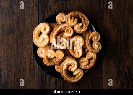 Palmier i cookie nella piastra nera su una superficie di legno. Concetto di dessert. Foto Stock