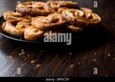 Palmier i cookie nella piastra nera su una superficie di legno. Concetto di dessert. Foto Stock