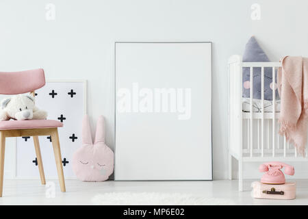 Il giocattolo di peluche rosa sulla sedia di legno accanto al poster di vuoto con mockup nella stanza del bambino interiore. Foto reale. Incolla il tuo poster qui Foto Stock