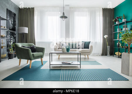 Sul tavolo verde e tappeto bianco in soggiorno spazioso interno con poltrona e divano Foto Stock