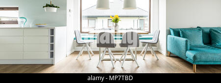 Panorama delle sedie grigio al tavolo con fiori di colore giallo accanto al divano blu in living room interior. Foto reale Foto Stock
