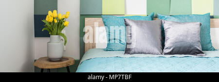 Panorama di coloratissimi interiore camera da letto con tulipani gialli sul tavolo di legno accanto al letto di blu. Foto reale Foto Stock