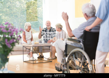 Gruppo di anziani la gente accogliente un amico seduti insieme in salotto Foto Stock