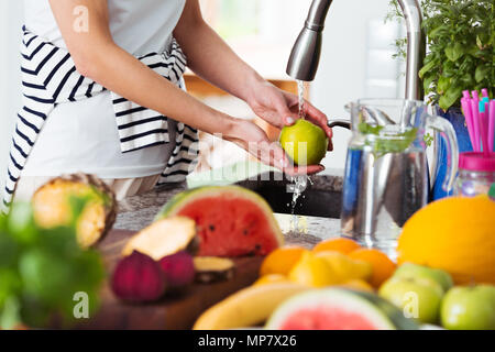 Donna sana il lavaggio un apple sopra lavello da cucina mentre prepara una colazione fresca con frutta Foto Stock