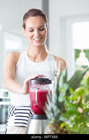 Donna sana in piedi in cucina e miscelazione frullato di barbabietole in blender per una fresca prima colazione Foto Stock