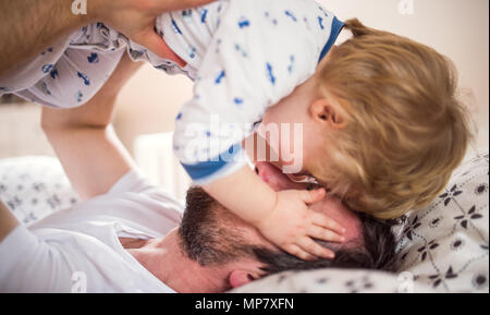 Padre con un bimbo piccolo ragazzo divertendosi in camera da letto a casa prima di andare a dormire. Foto Stock