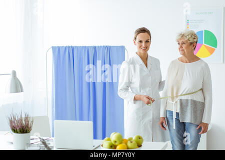 Sorridente nutrizionista paziente misura sulla dieta in ufficio per controllare lo stato di avanzamento Foto Stock