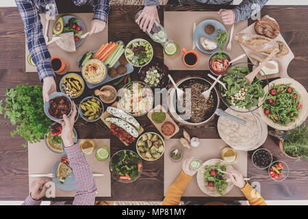 Amici gustando cibo vegetariano, seduti al tavolo rustico Foto Stock