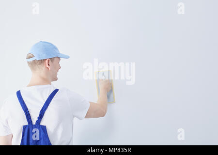 Giovane lavoratore edile preparare il muro bianco in casa per la verniciatura Foto Stock