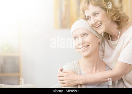 Sorridente donna più anziana che abbraccia il suo amico con il cancro che indossa una sciarpa Foto Stock