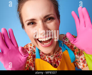 Grande tempo di pulizia. Sorridendo donna moderna in un grembiule giallo che mostra i guanti di gomma contro sfondo blu Foto Stock