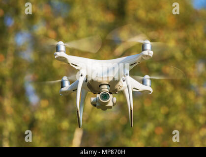 Un fantoccio DJI 4 Pro drone battenti, alberi in background, il fuoco selettivo sulla parte anteriore del drone Foto Stock