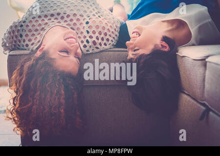 Tempo felice con il divertimento per un paio di giovane donna ridendo e sorridendo a casa a fissare il divano. migliori amici per sempre con i segreti del concetto. Foto Stock