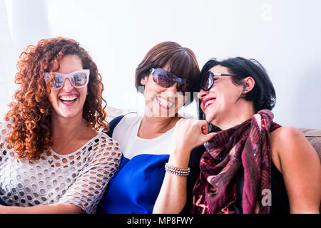 Tre giovani femmine crazy amici avente un sacco di divertimento a casa sul divano. tutti loro con occhiali da sole e laughi e sorrisi. in stretto contatto per il miglior f Foto Stock