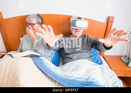 Persone adulte giovane divertirsi la mattina sul letto di casa. piscina divertente scena con la donna che ridere con un libro e un uomo con gli occhiali di protezione auricolare w Foto Stock