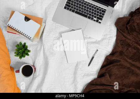 Caffè,notebook, pianta in vaso e pila di libri sul letto. Area di lavoro del letto. Foto Stock