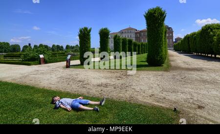 La Venaria Reale, Regione Piemonte, Italia. Giugno 2017. I turisti di esplorare il magnifico parco del palazzo. Un giovane turista è in appoggio sull'erba. Foto Stock